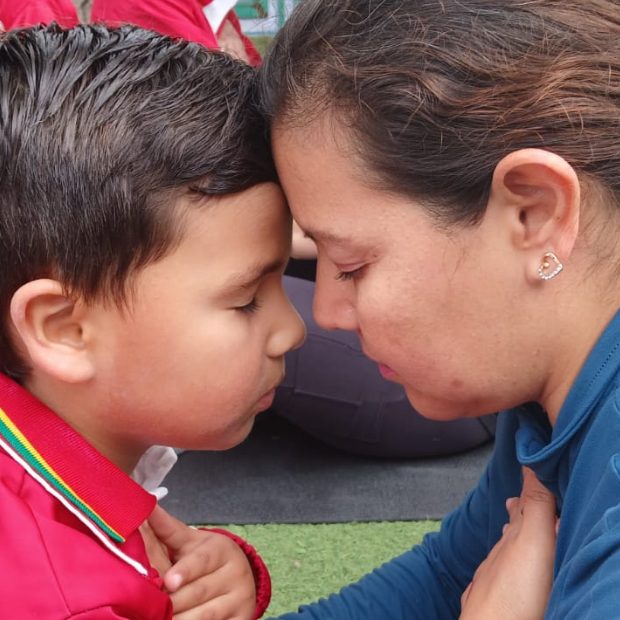 Maestra de Reguilete abrazando a un niño y hablando con él a la altura de sus ojos