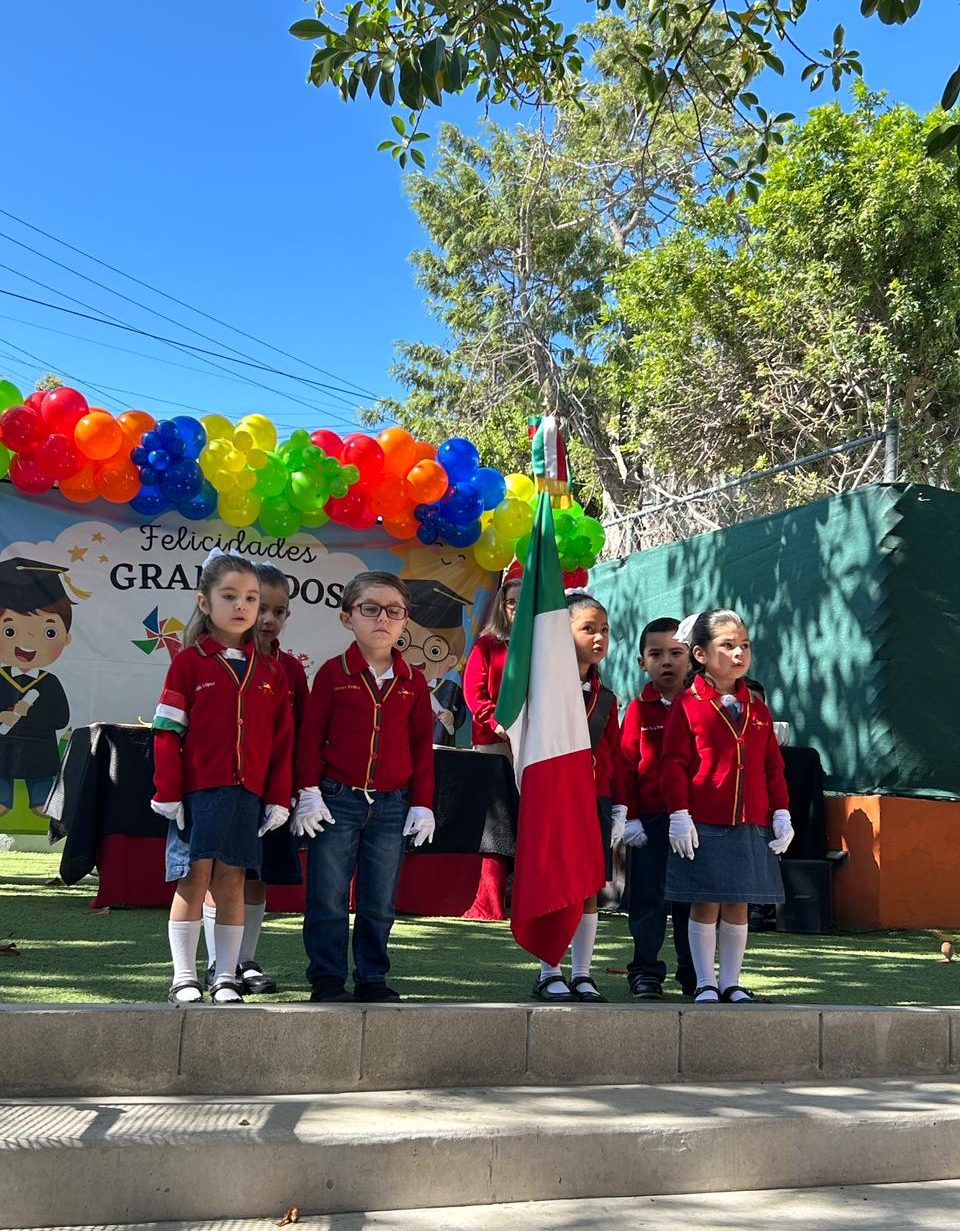 Escolta de alumnos de tercero de preescolar durante un honor a la bandera en el patio de Reguilete