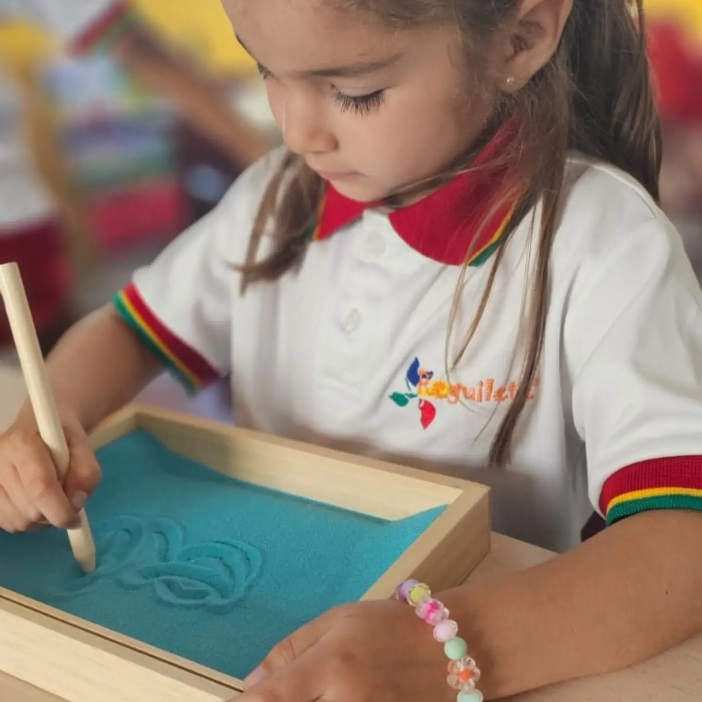 Niña de preescolar trazando con un punzón sobre una charola de arena del material Montessori