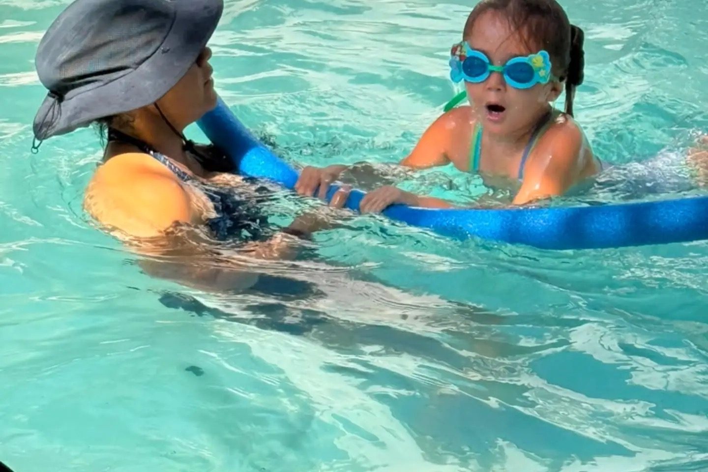 Dos niñas aprendiendo a nadar con flotador acompañadas por una instructora en la alberca