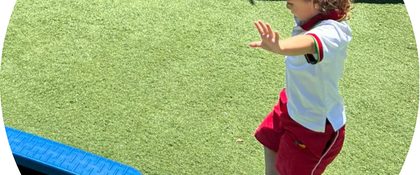 Niña caminando con los brazos abiertos sobre una viga de equilibrio en la clase de educación física
