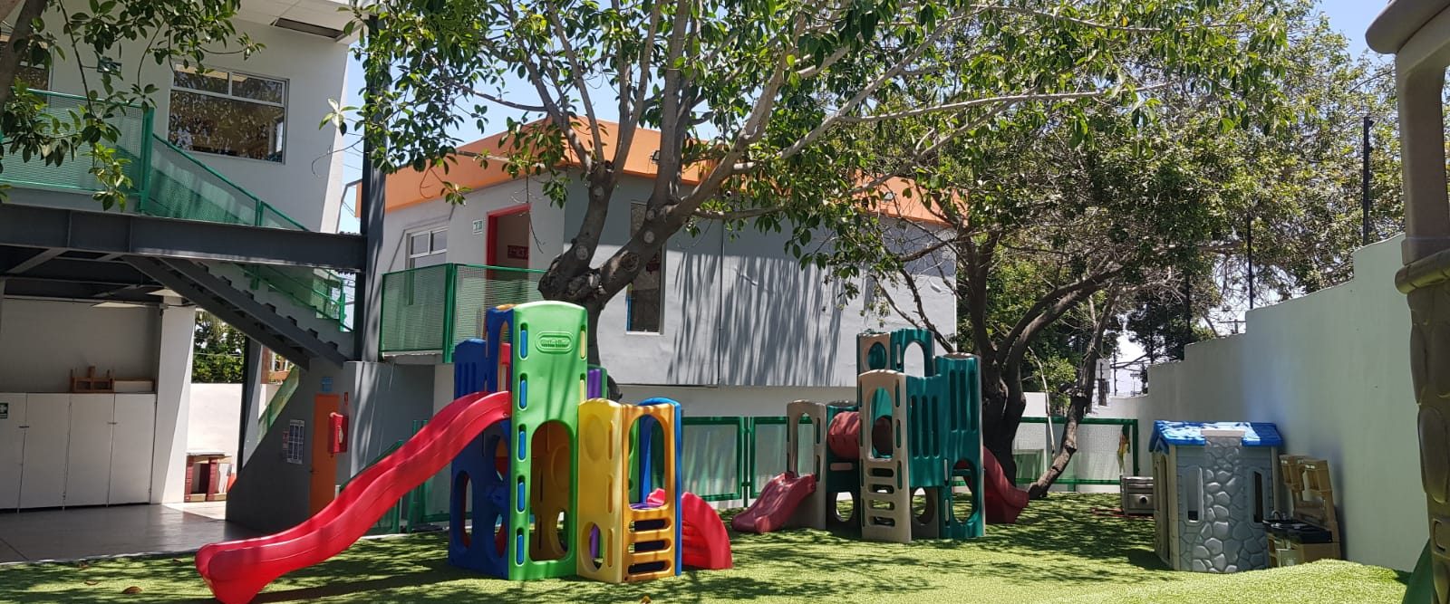 Patio de Reguilete con pasto sintético, juegos infantiles de colores y un árbol grande dando sombra