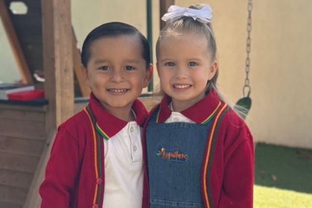 Dos alumnos de preescolar con el uniforme de Reguilete junto a los columpios del patio